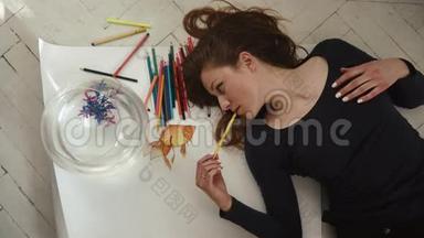 可爱的年轻女艺术家在白色背景上拍摄一张<strong>小金鱼</strong>的照片。 顶部视图